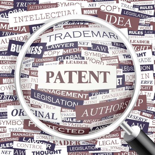 Magnifying glass over a collage of intellectual property terms centered on PATENT