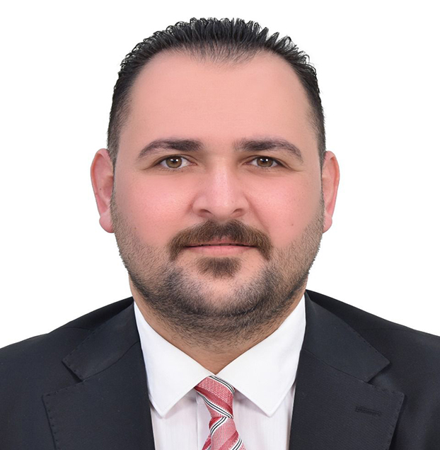 Professional headshot of a man with dark hair and a trimmed beard, wearing a black suit and pink striped tie, facing the camera against a white background.