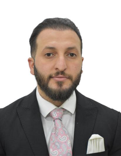 Portrait of a man in a black suit with a white shirt and pink paisley tie, looking at the camera.